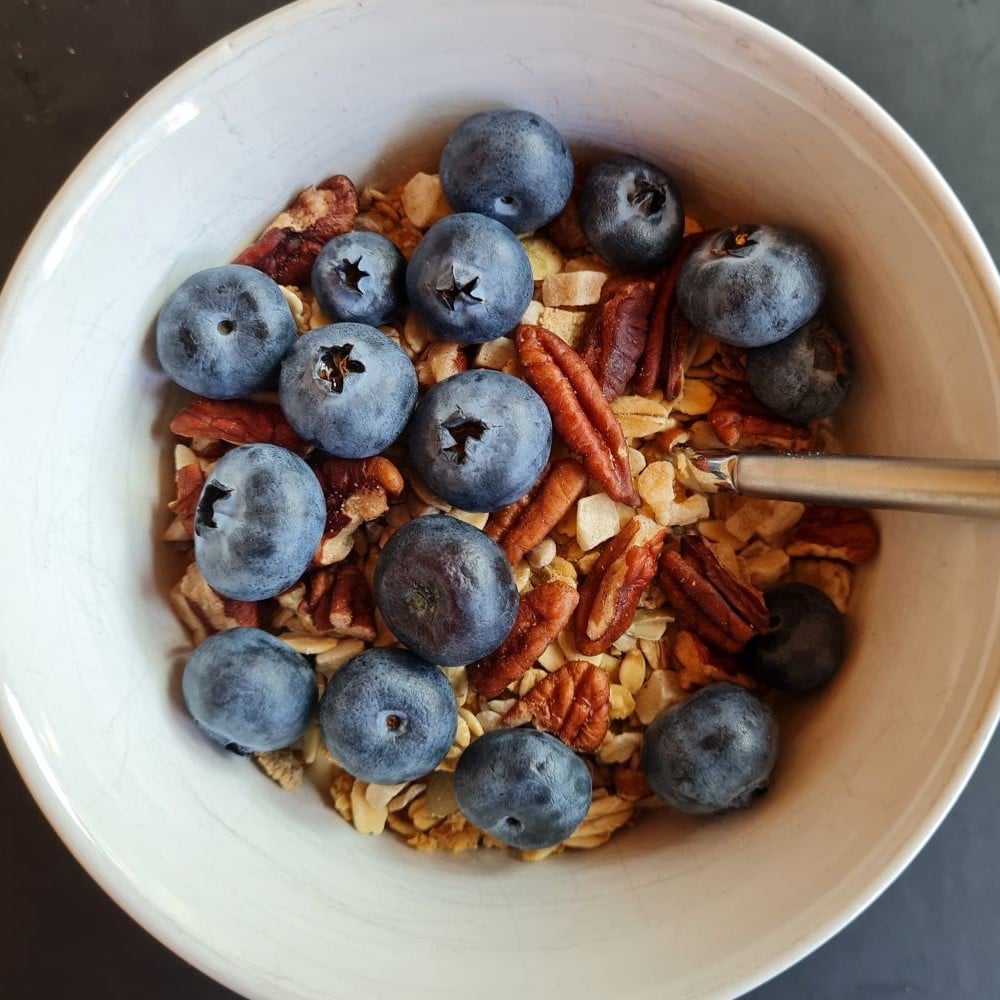 Soyayoghurt (m mango - uden tilsat sukker) m glutenfri mysli, pekannødder og blåbær i hvid skål