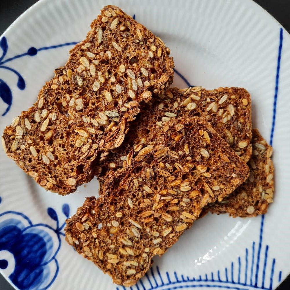 4 tynde skiver glutenfrit rugbrød fyldt med forskellige kerner og frø.. Brødet er ristet og ligger lidt tilfældigt på en megamussel tallerken