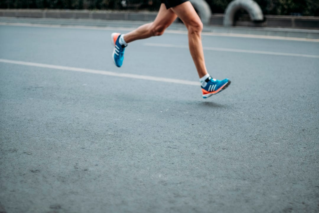 Marathonkvinden illustreret ved kvinde i løb på asfaltvej. Man ser kun benene. Hun har turkise løbesko på.