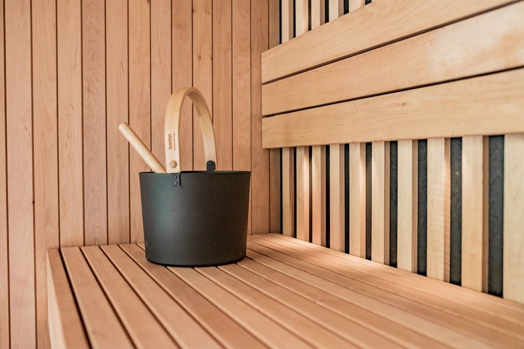 Saunatæppe symboliseret ved del af interiør fra sauna. Man ser spand til vand med øse, stående på en indbygget saunabænk.