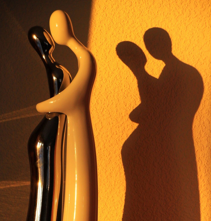 Seksuelle bivirkninger symboliseret ved stilistisk figur af kvinde og mand i omfavnelse. Han i lyst materiale og hun i stålagtigt. De kaster skygger på gullig baggrund.