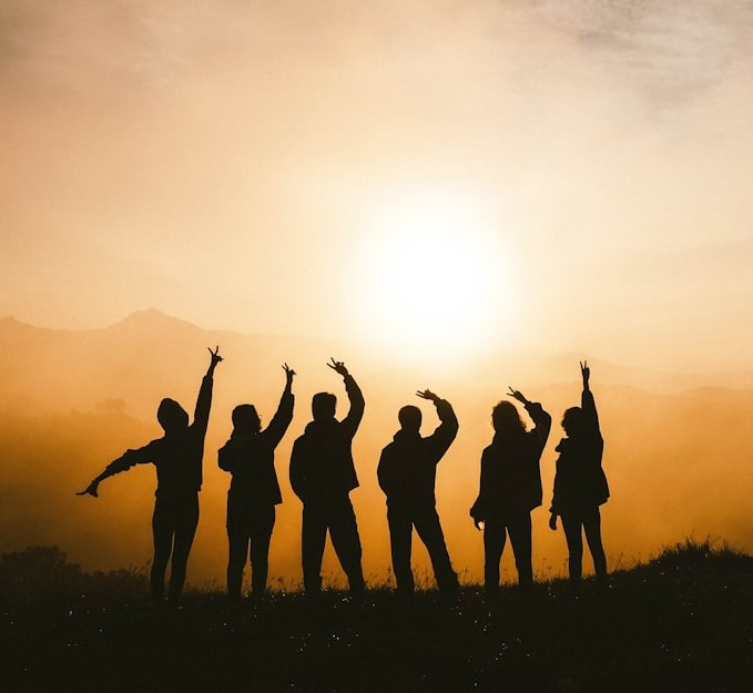 Sociale grupper symboliseret ved 6 mennesker der står på rad i silhuet med solopgang eller solnedgang og laver mønster med armene.