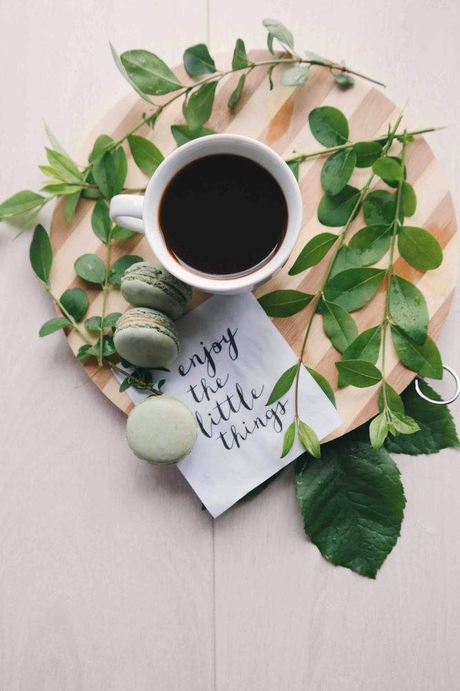 Taknemmelighed symboliseret ved en kop kaffe, nogle grønne macarons-småkager og en lille note med teksten: Enjoy the little things - Nyd de små ting i livet.