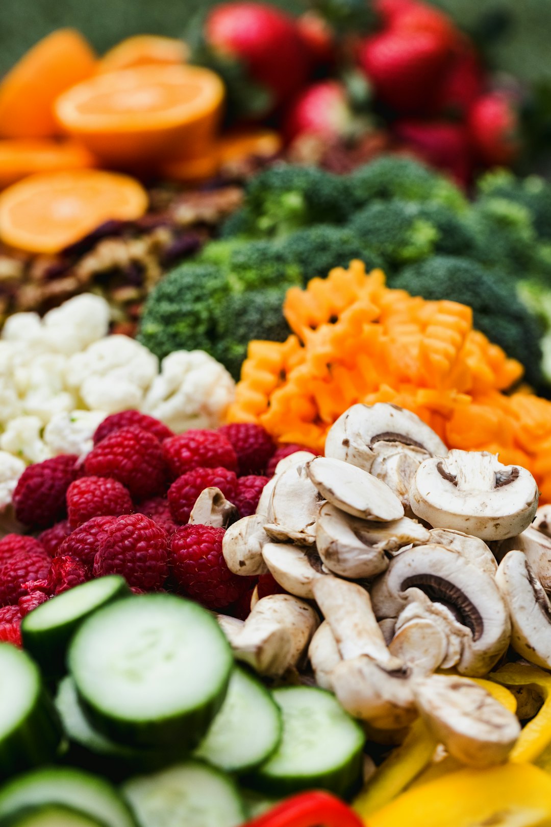 Antiinflammatorisk kost illustreret ved rå grøntsager som champignons i skiver, hindbær, agurk, majs, blomkål, broccoli, appelsin mm.