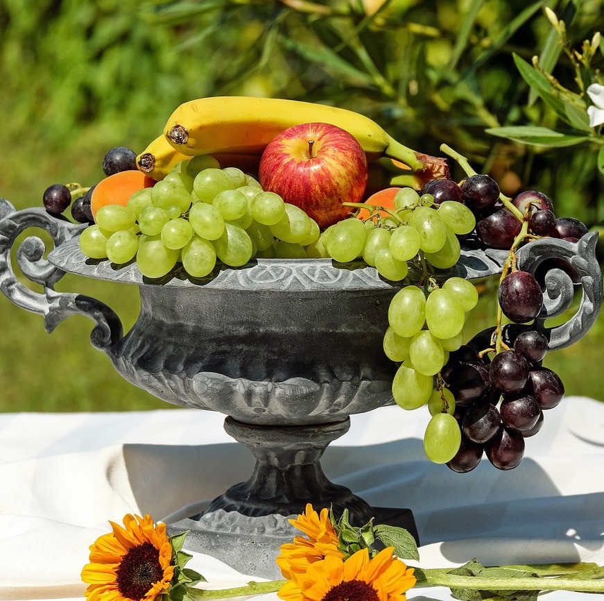 Børn og unge med kræft symboliseret ved en opsats i gråt metal med et par solsikke blomster foran. Og fylde med frugt som druer, æbler og banan.