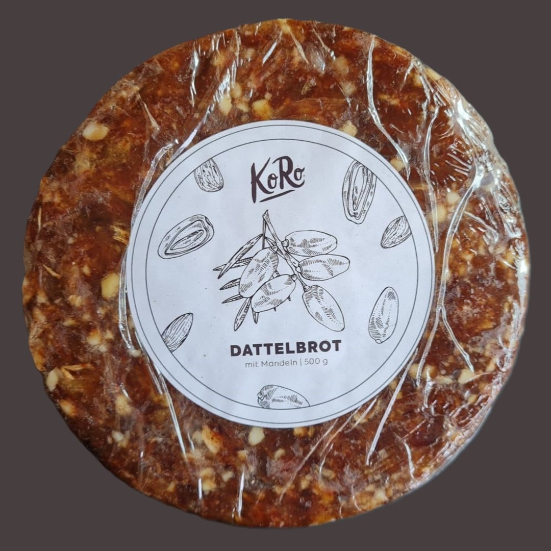 Dadel-nøddebrød med flad rund form i cellofanindpakning med hvid rund etiket.
