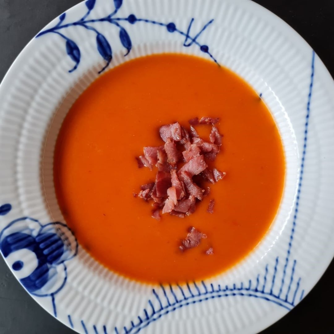 Rød suppe med drys af kalkunbacon-tern i midten. Ophældt i dyb megamussel tallerken.