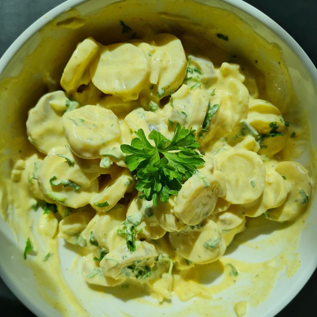 Kartoffel- jordskokkesalat symboliseret ved hvid skål med salat af nævnte. et lille drys persille på toppen.