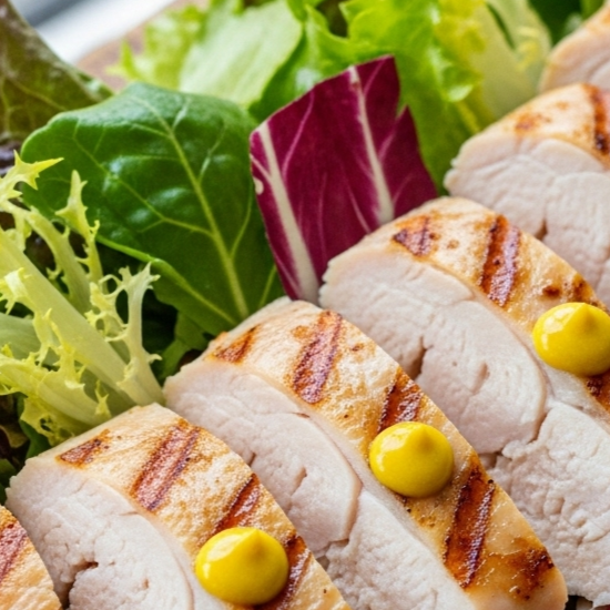 Morgenmad og frokost symboliseret ved skiver af kyllingbryst med en lille tut sennep på hver skive og liggende på en bund af salat.