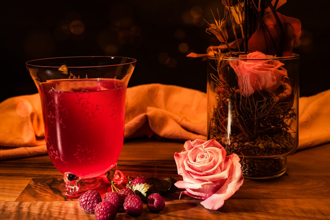 Nedsat appetit symboliseret ved et glas med saft. Hindbær i forgrunden. Ved siden af er bordet pyntet med rose og borddekoration. I baggrunden ligger en gul-orange stofserviet nonchalant sammenfoldet.
