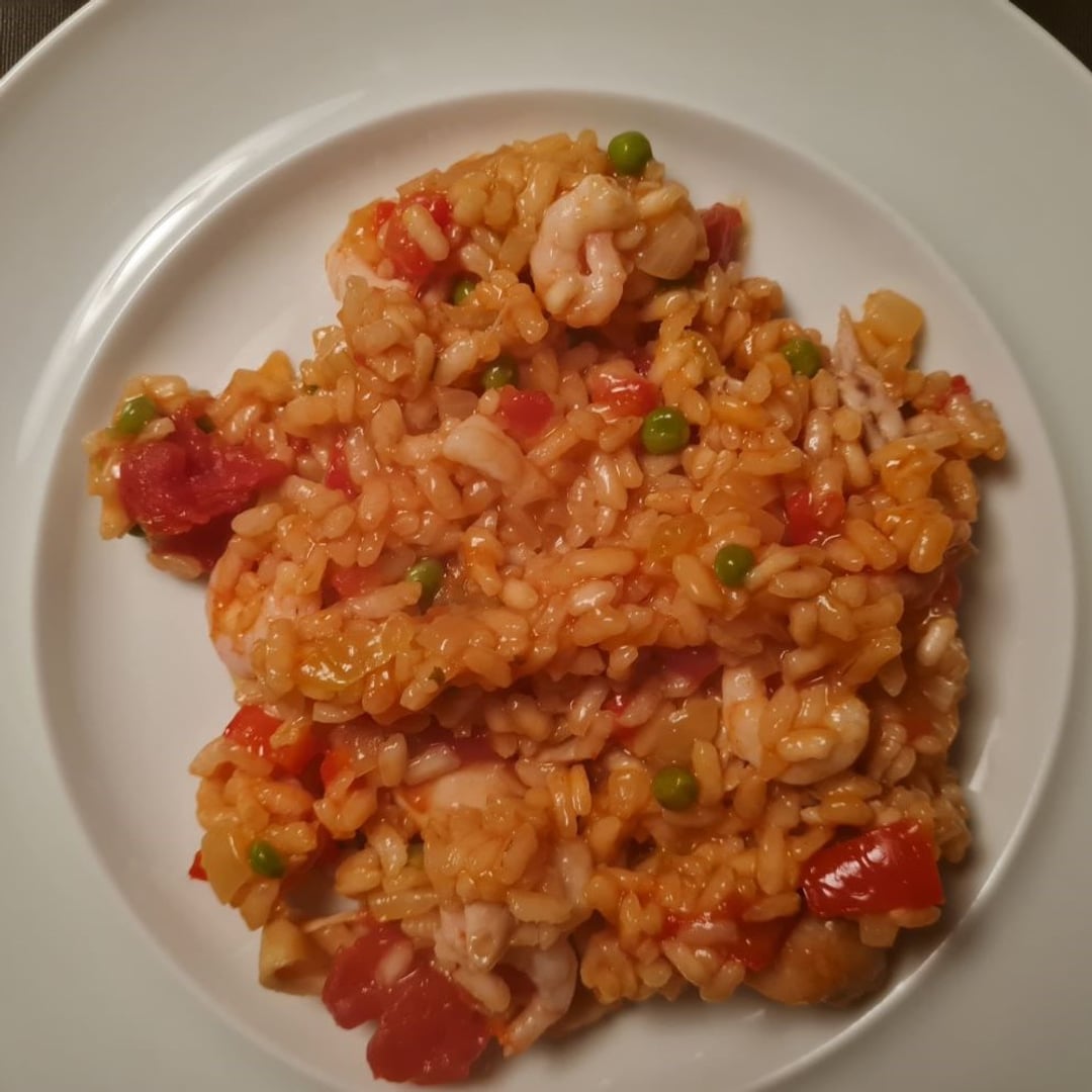 Paella m rejer, tun, løg, hvidløg, tomat, rød peber og ærter på hvid tallerken.