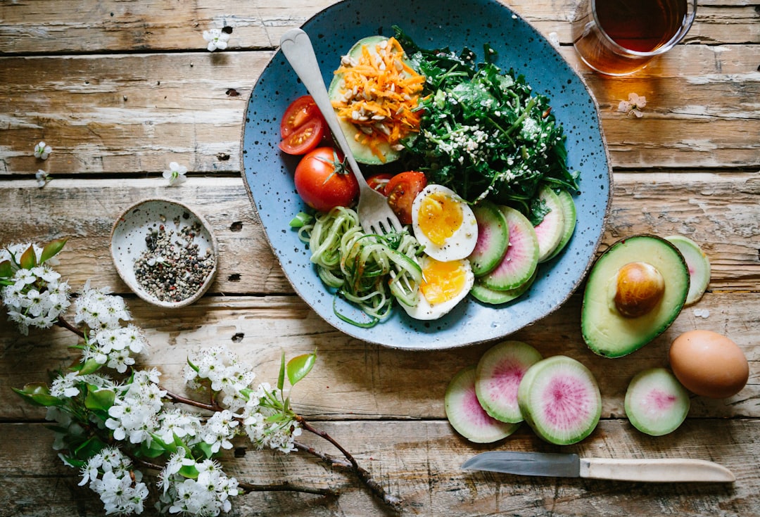 Plantebaseret kost symboliseret ved en rustik tallerken med tomater, halve æg, spinat, spirer og skiver fra frisk figen. I forgrunden ligger halve avocados og skiver fra figen samt et helt æg med skal. Desuden ligger der en blomstrende gren fra frugttræ.