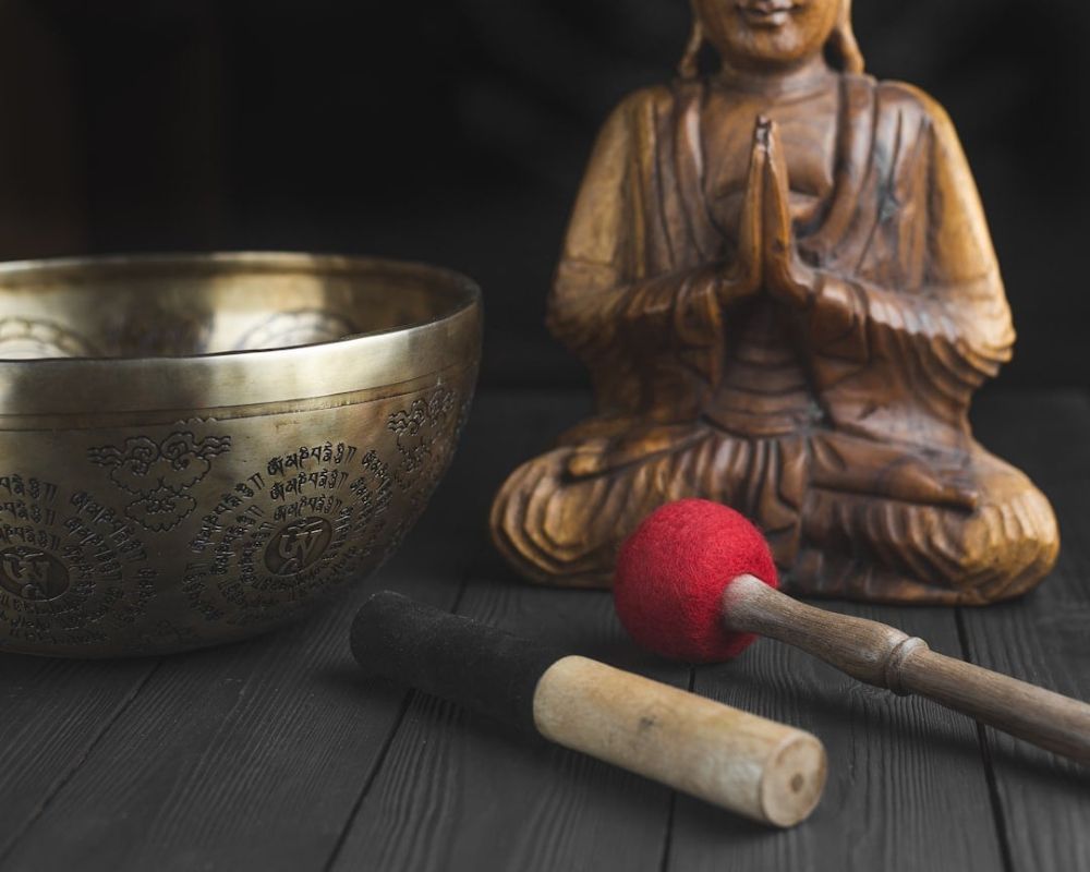 Resonansbehandling symboliseret ved en ornamenteret messingskål og en buddha-figur i ben og 2 forskellige knebler i forgrunden.