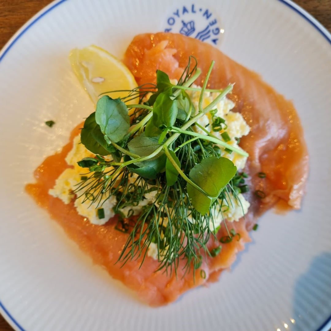Frokostmad med rigeligt røget laks. Herover røræg. Pyntet med purløg og ærtespirer, samt lille citronbåd.