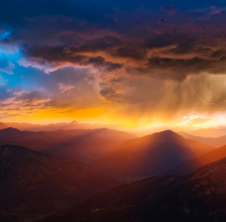 Strålebehandling symboliseret ved solnedgang over bjerge. Dramatiske skyformationer og et lille stykke klar blå himmel.