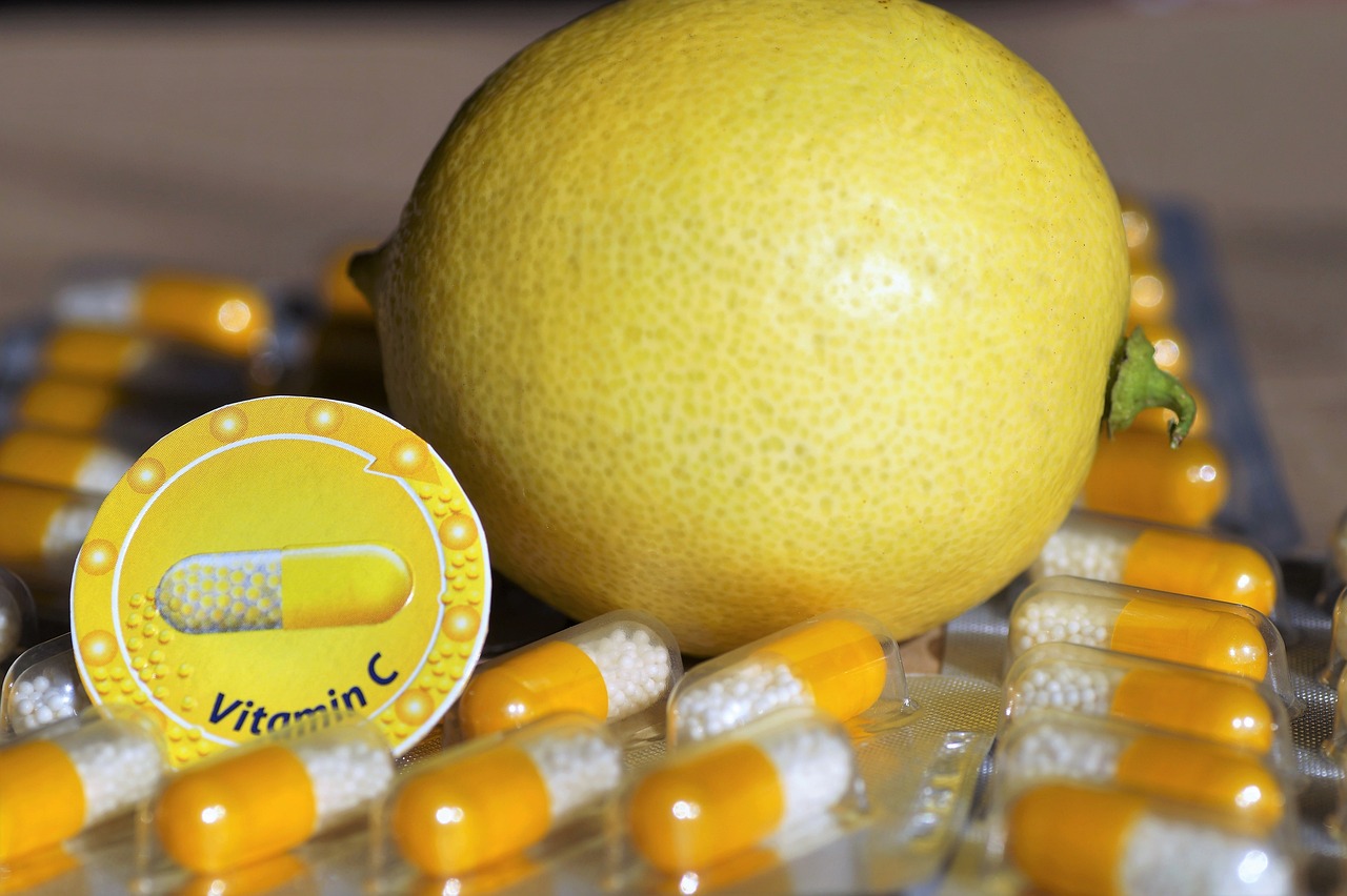 Vitamin-C oralt symboliseret ved et par citroner og nogle hvide og orange kapsler foran.