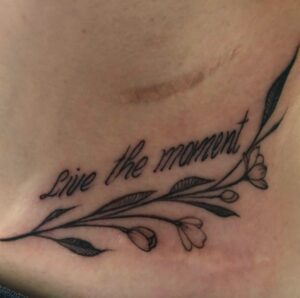 Lisa Pascale Reynolds Stahlschmidts tatovering viser en blomstergren med inskriptionen: Live the moment i skråskrift over.