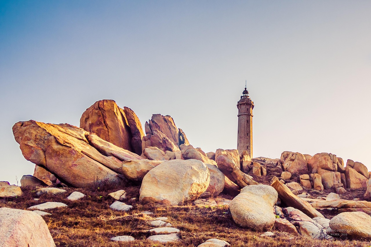 Chris Beat Cancer symboliseret ved øde og tørt, stenet landskab med et fyrtårn i baggrund. Farverne er brune mod dæmpet grå-blå himmel.