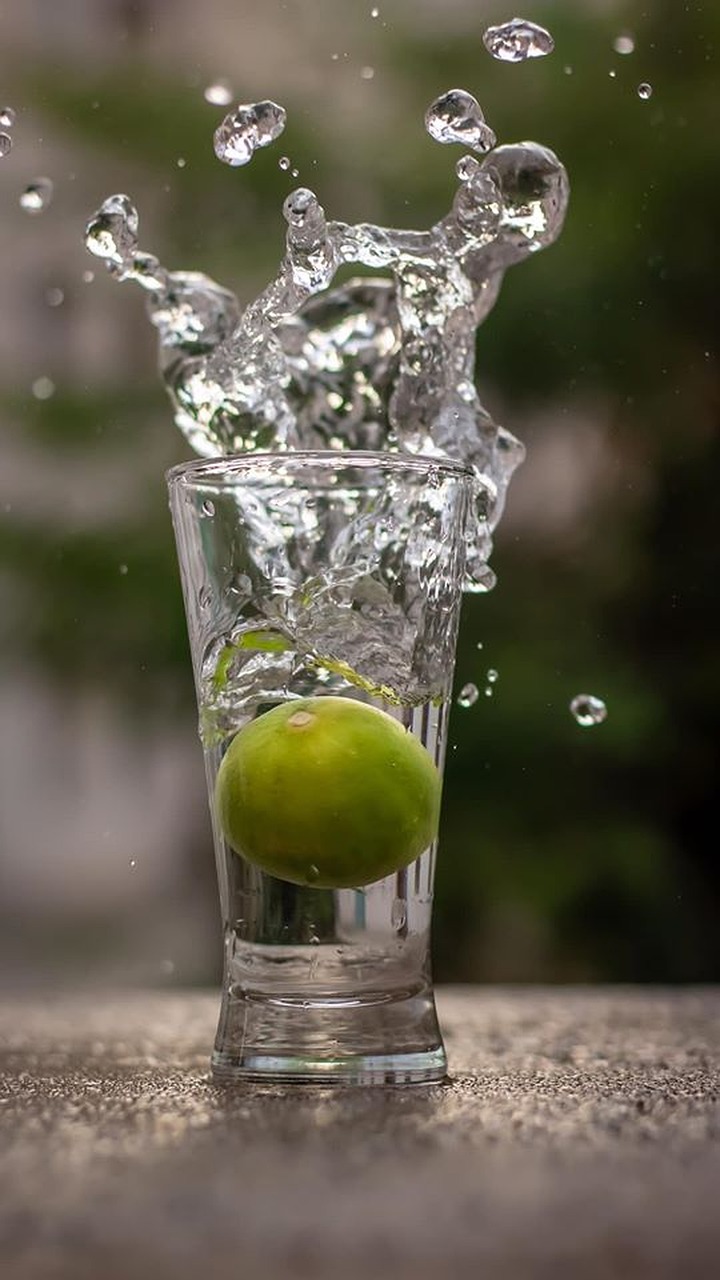 Detox - afgiftning symboliseret ved klart glas med vand, hvor der smides en grøn frugt ned, så vandet sprøjter dekorativt op af glasset.