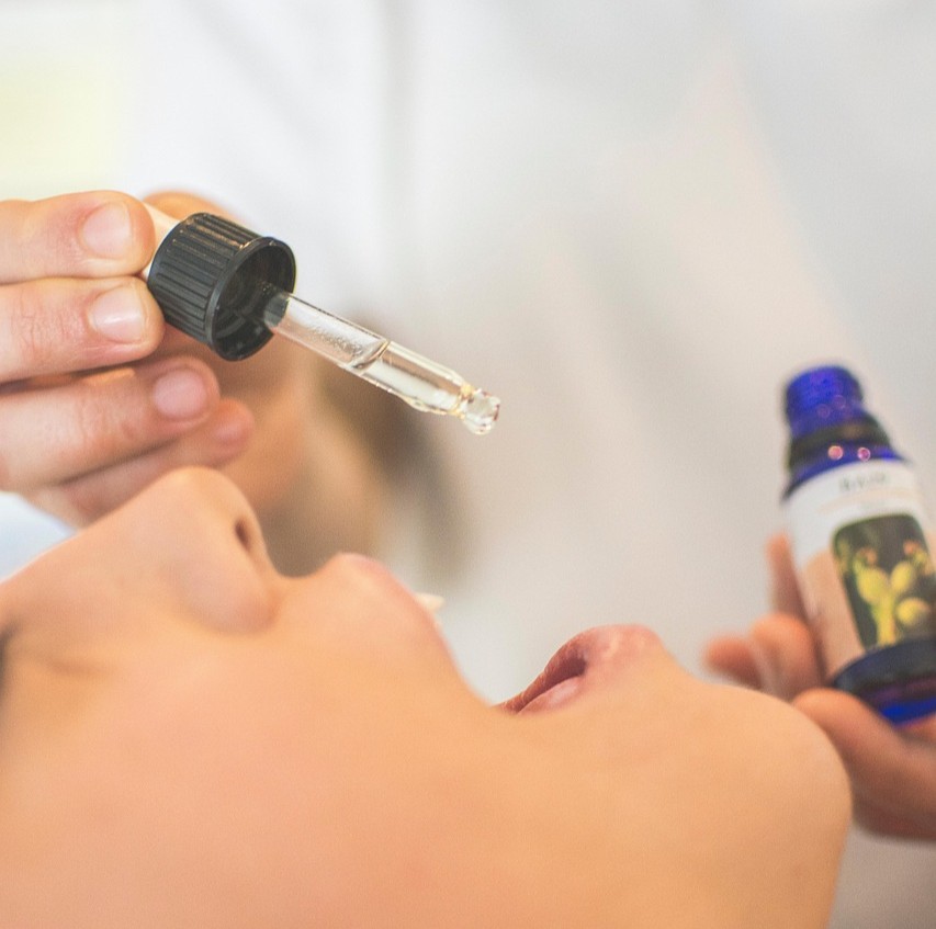 Bachs Blomsterremedier symboliseret ved del af et ansigt med åben mund og en flaske og en pipette, der er ved at give dråber i munden.