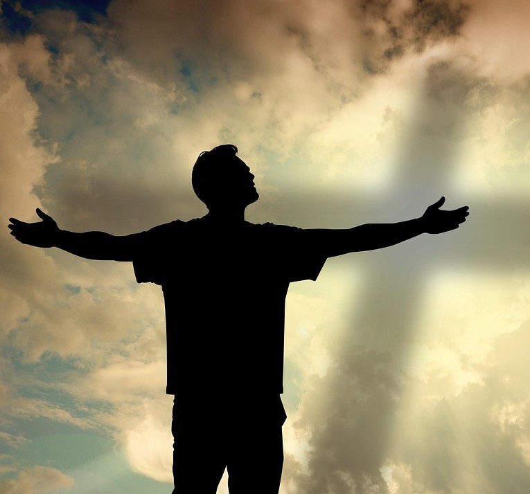 Taknemmelighed og kærlighed symboliseret som silhuetten af en mand, der står med armene strakt ud til siden og ser mod en hvid himmel, hvor hans skygge danner et kors.