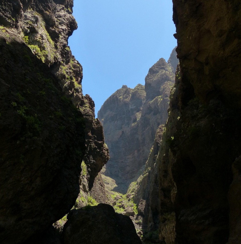 Livskvalitet og medansvar symboliseret ved en kløft mellem to høje klipper. Man ser bjerg i baggrunden og blå himmel.