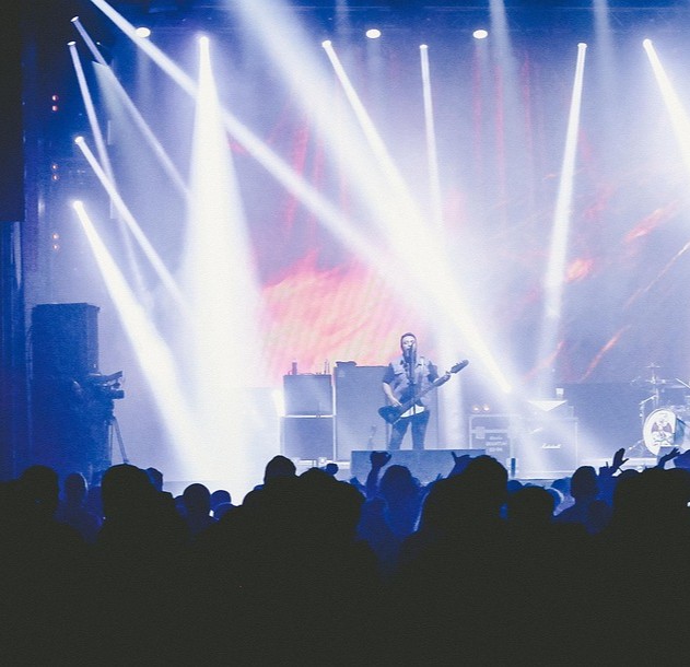 Lys- og støjforurening symboliseret ved massive hvide lyskegler der rettes ud i rummet. Ser ud til at være fra en koncert. Silhuetter af mennesker i forgrunden.