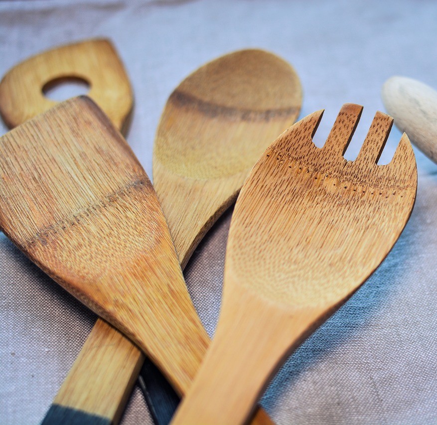 Køkkenudstyr, madopbevaring og emballage symboliseret ved grydeskeer og salatsæt i træ.