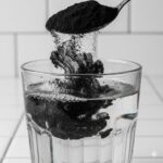 Aktivt kul symboliseret ved et klart glas med vand, hvor der kommes en spiseske kulpulver ned i.