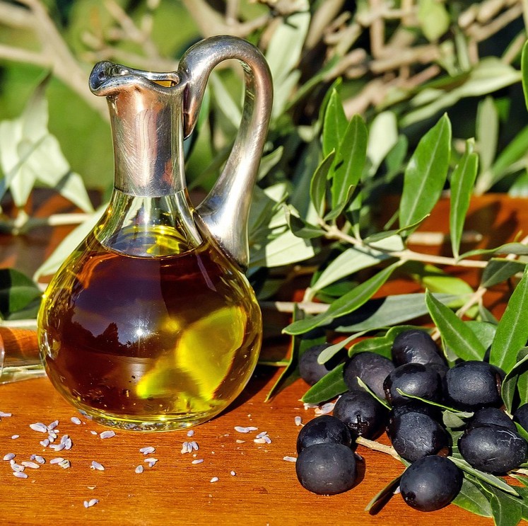 Makronæringsstoffer og kræft symboliseret ved en hældeflaske med olie og nogle sorte oliven ved siden af denne, samt olivengrene.