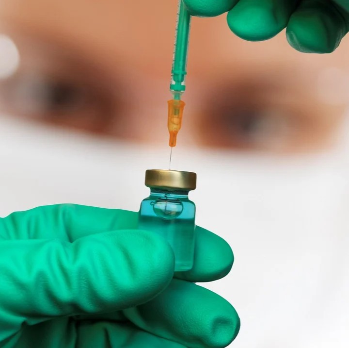 Vaccination - for og imod symboliseret ved dele af et sæt hænder med grønne handsker, der trækker væske op fra i en sprøjte fra et hætteglas.