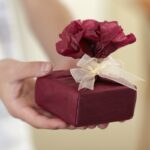 Gaver symboliseret ved en hånd der rækker en pakke i rødt silke.gavepapir.