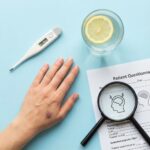 Essentiel Trombocytose symboliseret ved en hånd, et termometer, et glas vand med citron og et forstørrelsesglas over et ark med tekst.