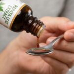 Papaya bladekstrakt symboliseret ved en teske, hvor der hældes væske op fra en brun glasflaske.