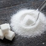 D-Mannose symboliseret ved noget hvidt pulver og nogle firkantede huggede stykker på et bord.