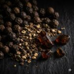 Piperin symboliseret ved sorte peberkorn og nogle brune krystaller.