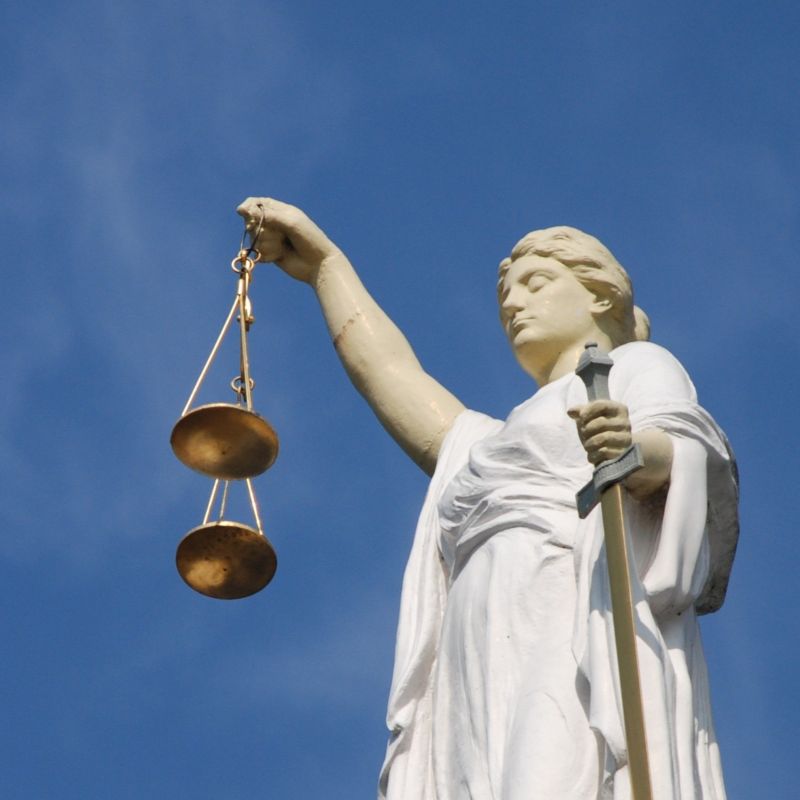 Patientvejleder og dine rettigheder symboliseret ved en justice-skulptur med vægte holdt op mod blå himmel.